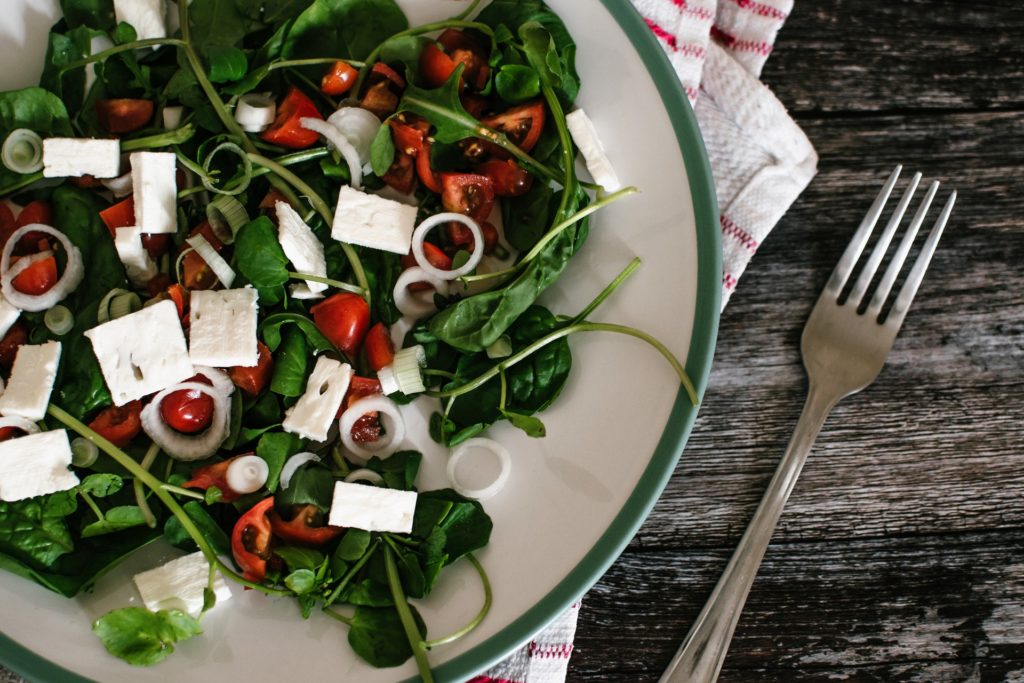 A white plate that is full of veggies and feta cheese